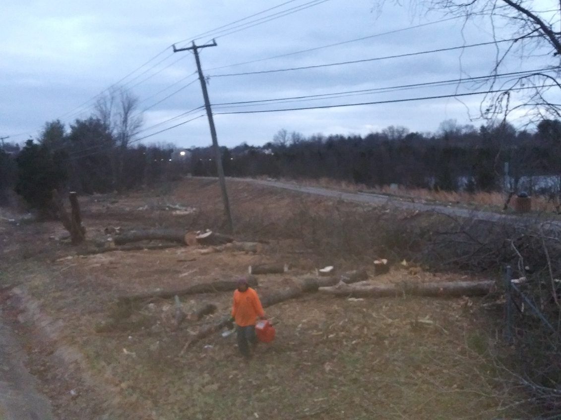 A man in an orange jacket is carrying a gas can in a field.