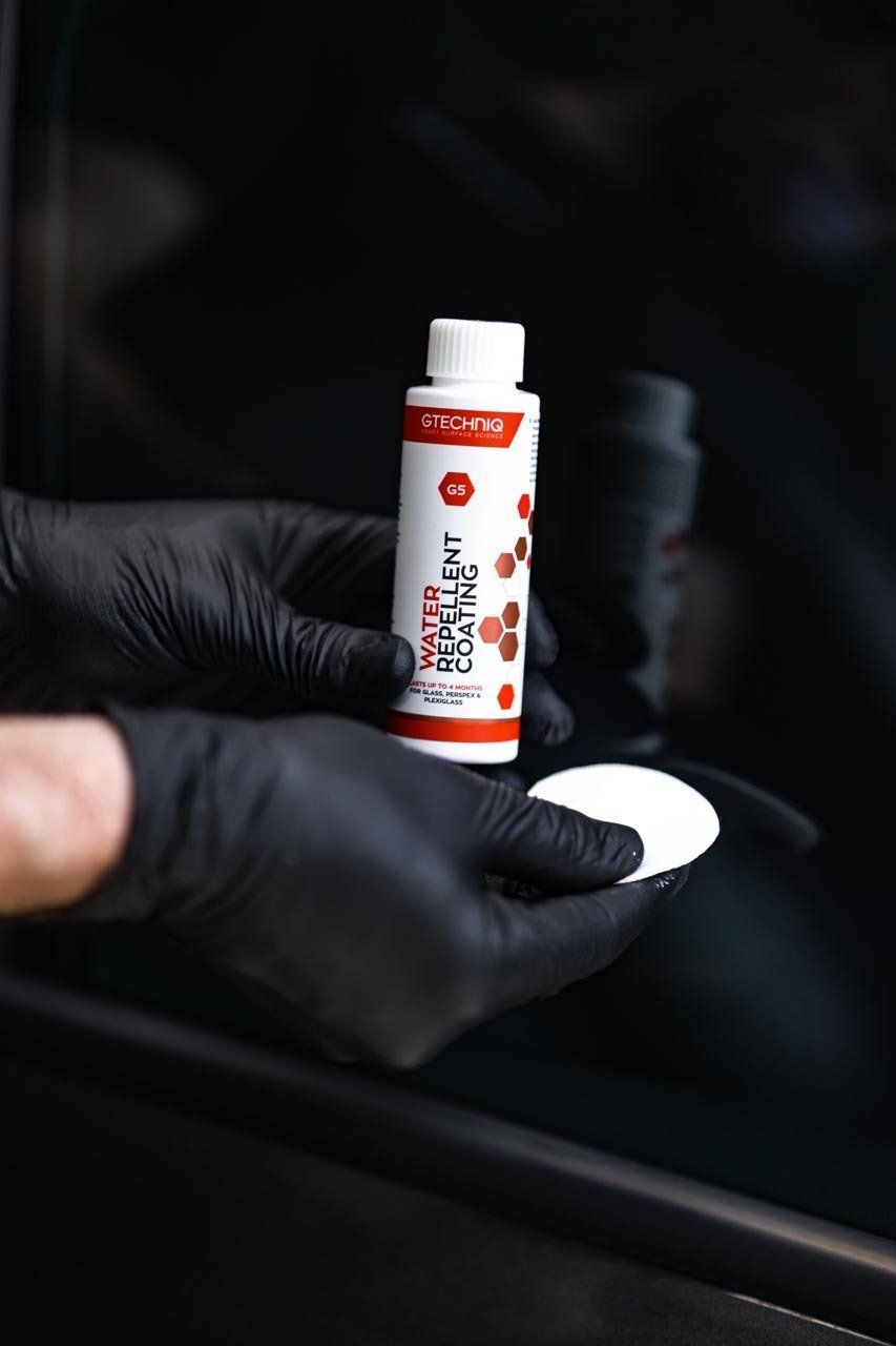 Gloved hands hold a small red-and-white bottle beside a white cap in a dark setting