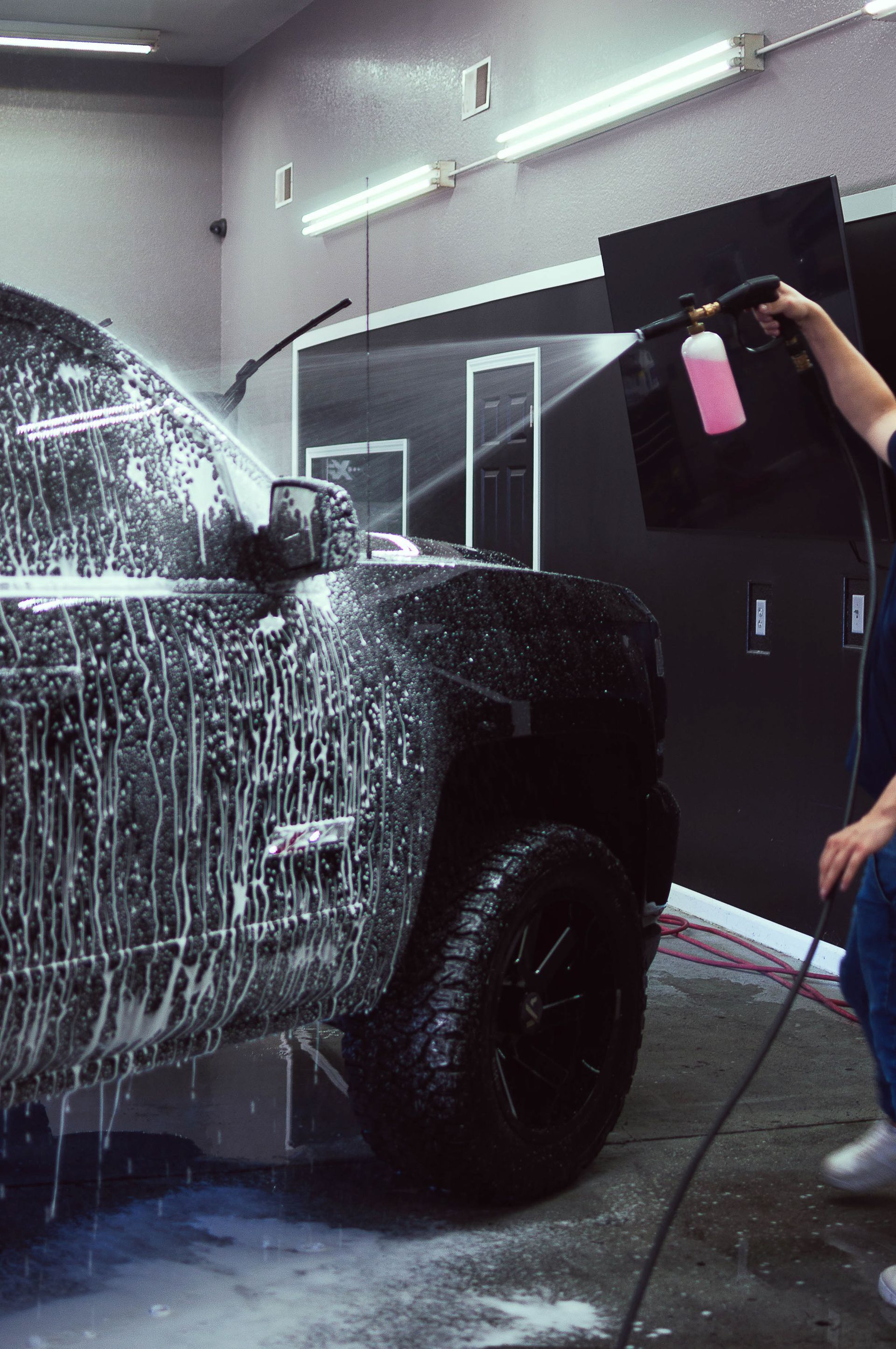 Person spraying foam onto a black pickup truck in a car wash bay