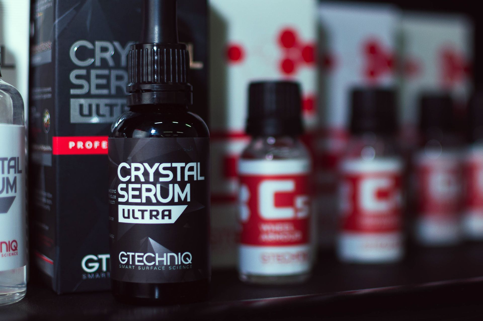 Black GT Technic Crystal Serum Ultra bottle with blurred red bottles in the background
