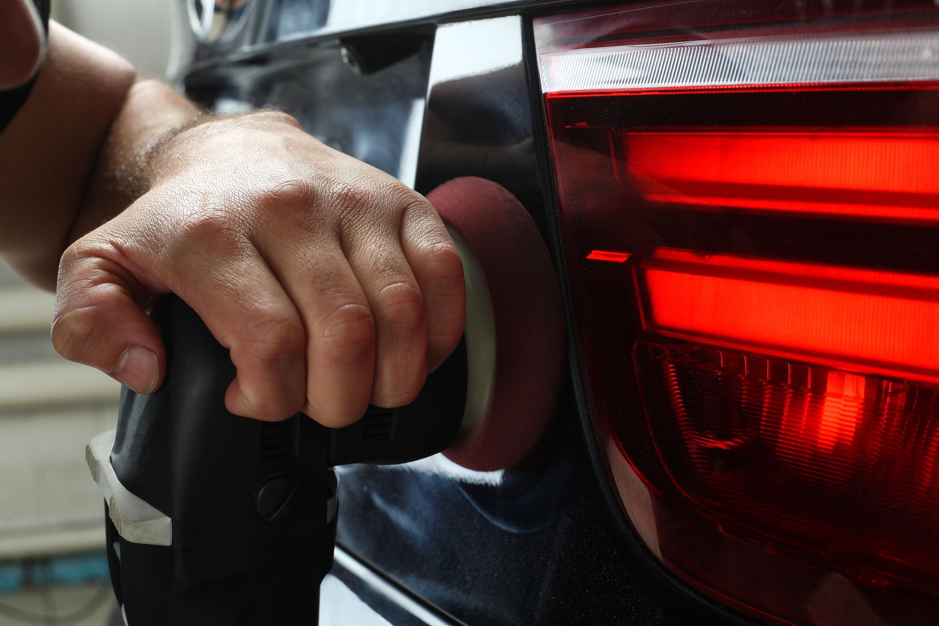Hand holding a charging plug connected to a car’s rear charging port, with red taillights visible