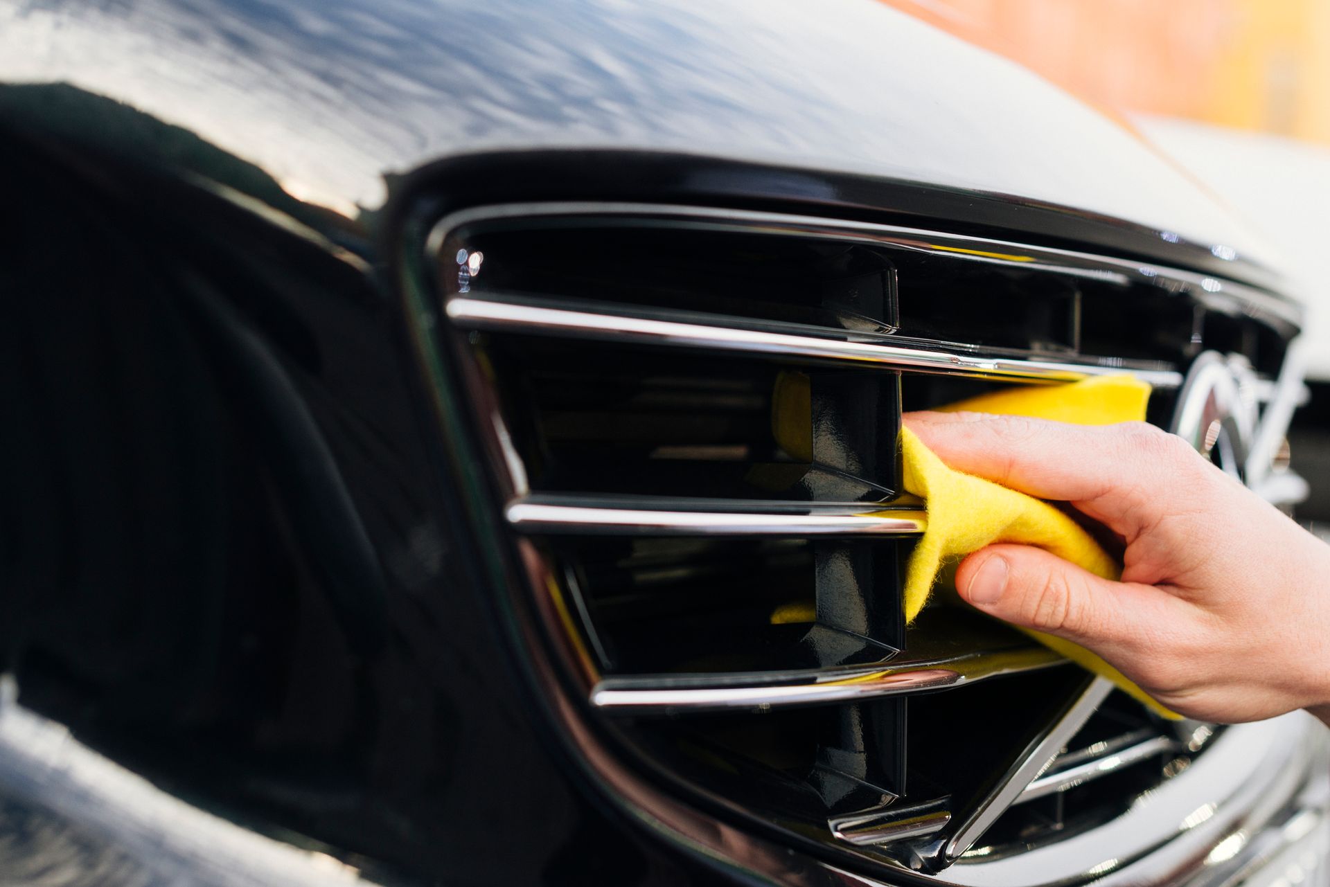 Hand cleaning a car’s chrome grille with a yellow cloth