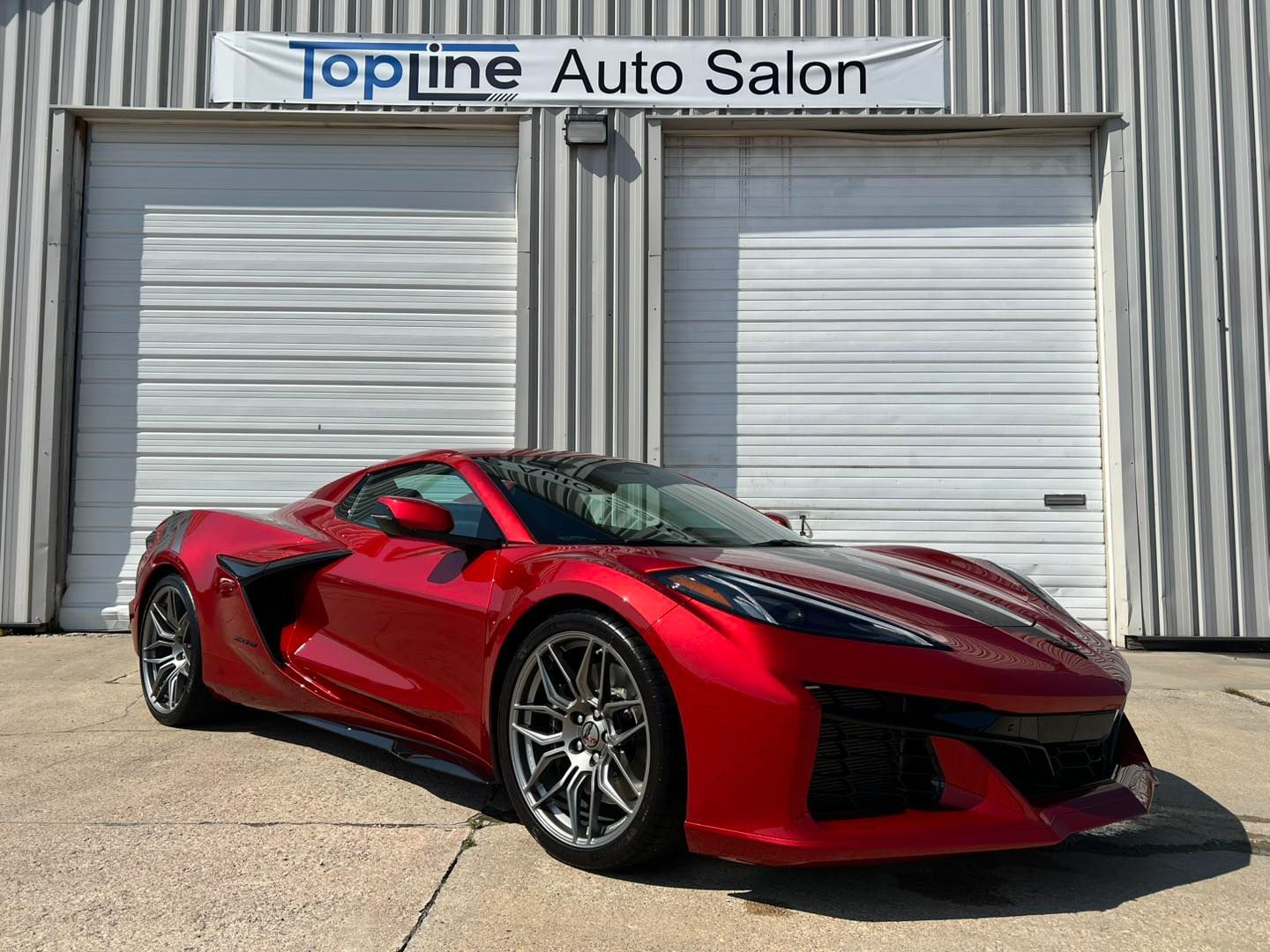 Red sports car parked outside Topline Auto Salon with closed garage doors in the background