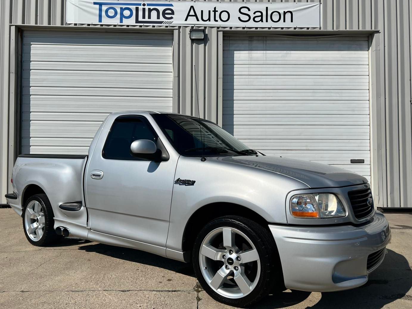 Silver pickup truck parked outside Topline Auto Salon showroom doors