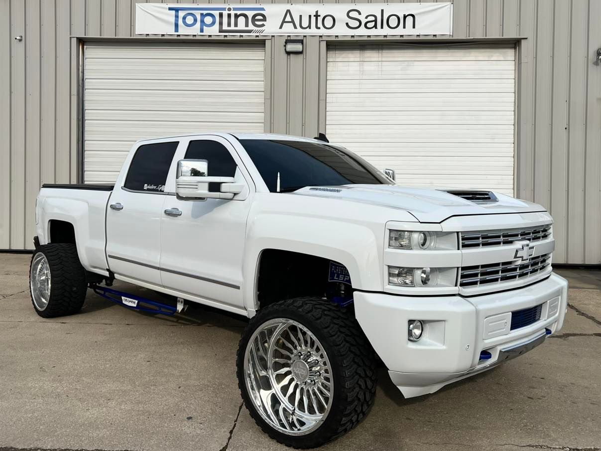 White lifted pickup truck parked in front of Topline Auto Salon