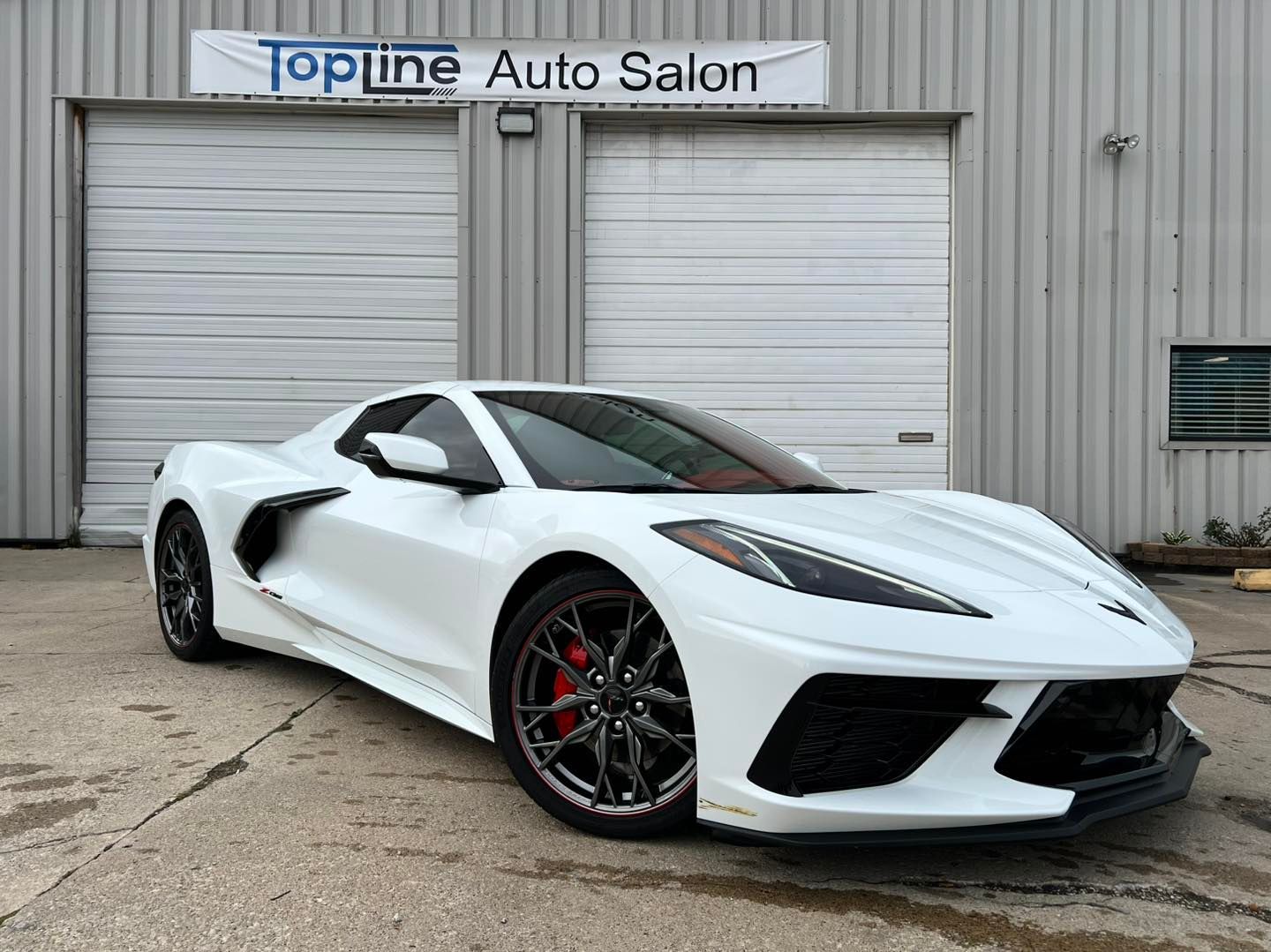 White sports car parked outside Topline Auto Salon garage doors