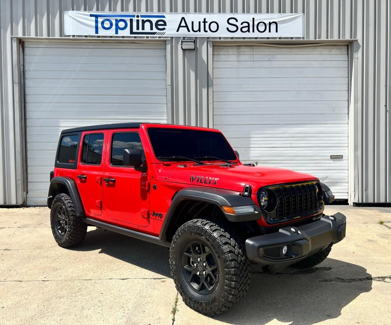 Red Jeep Wrangler parked in front of Topline Auto Salon garage doors