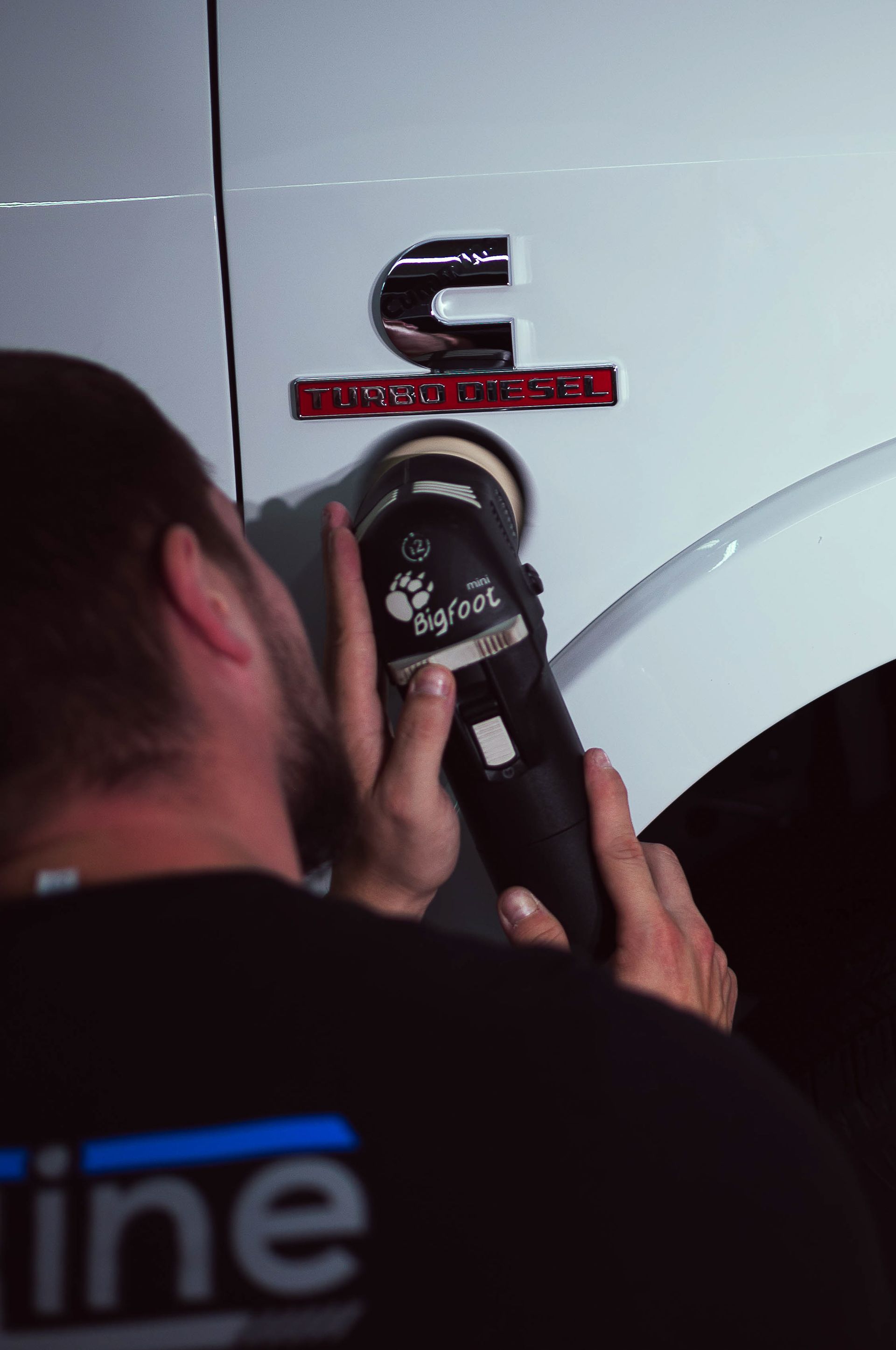 Person using a handheld tool to polish a white car panel near a chrome emblem
