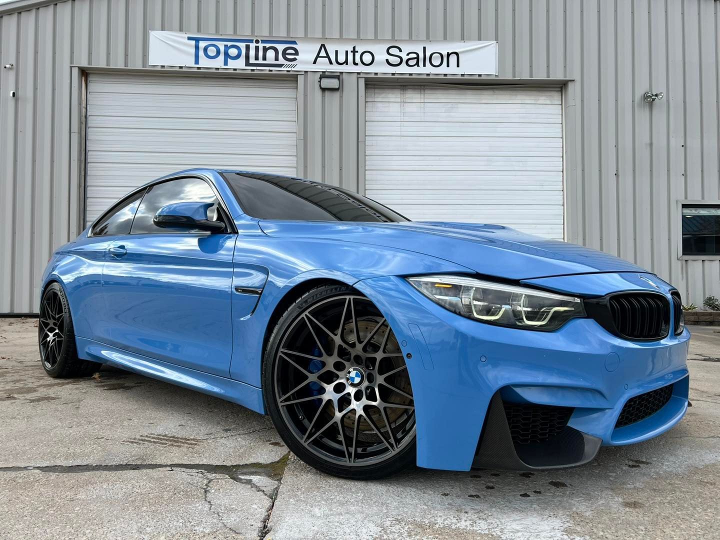 Blue sports coupe parked outside Topline Auto Salon garage, front three-quarter view