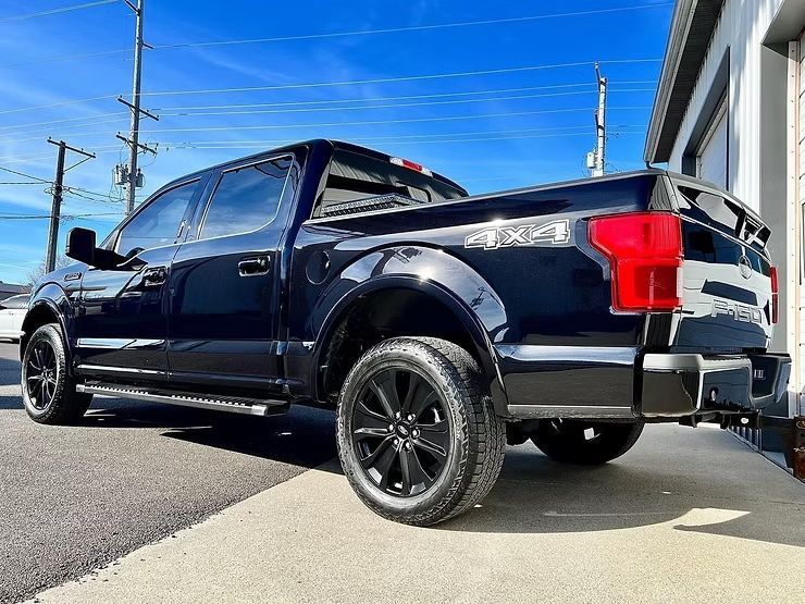 Black pickup truck parked beside a building under a bright blue sky
