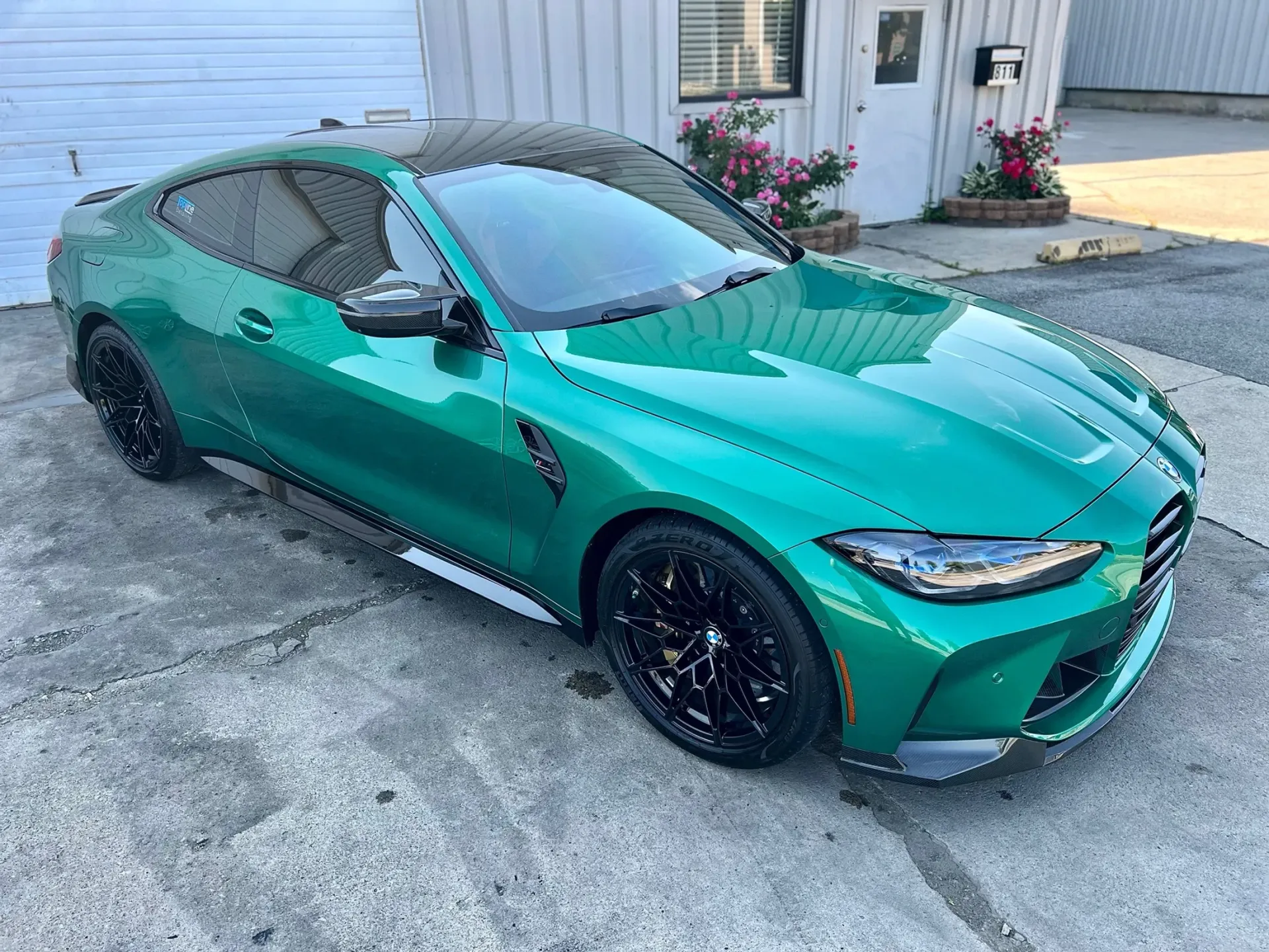 Teal BMW coupe parked on a driveway beside a house.