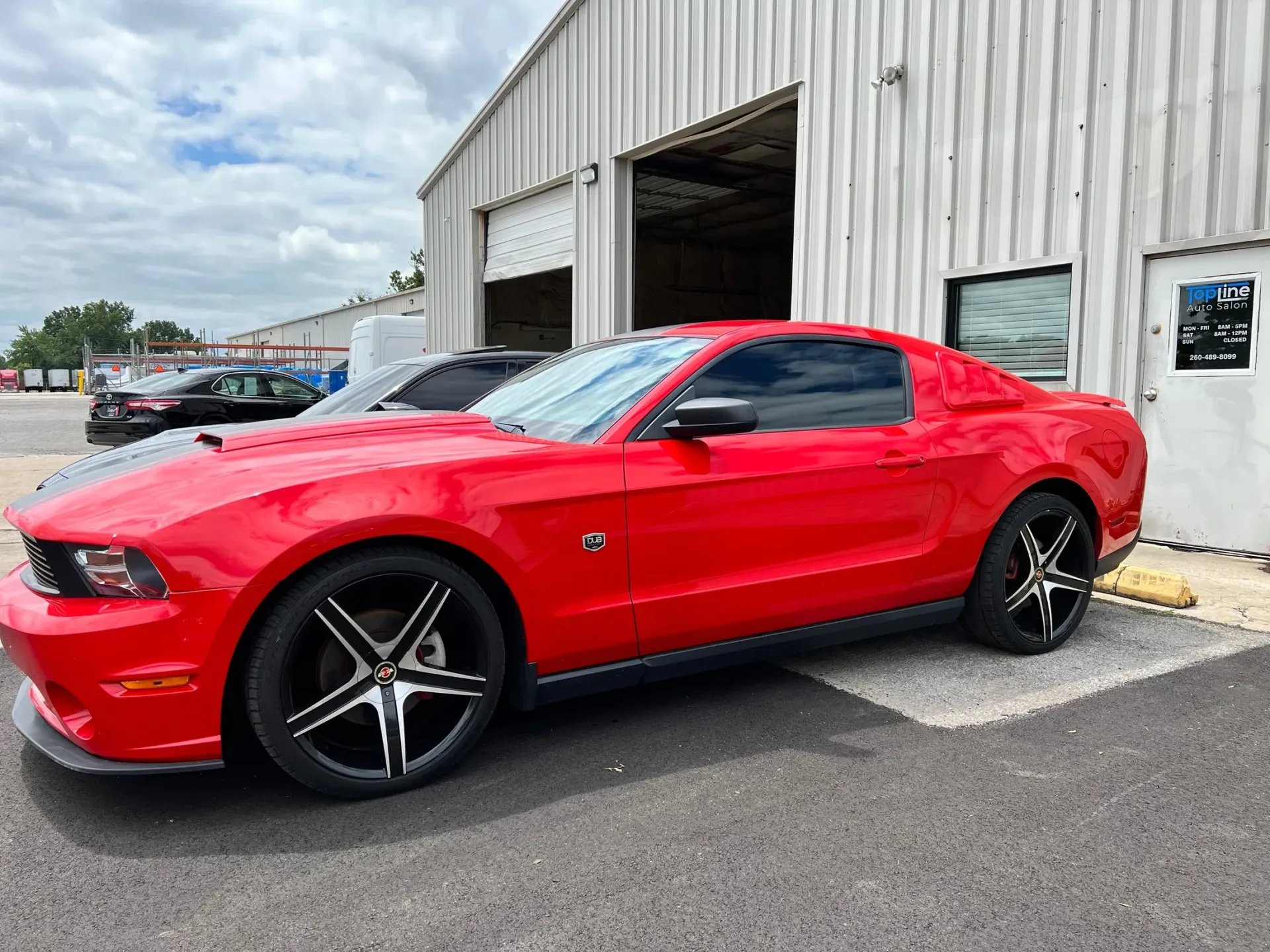 Red sports coupe parked outside an auto shop, with a large open garage door