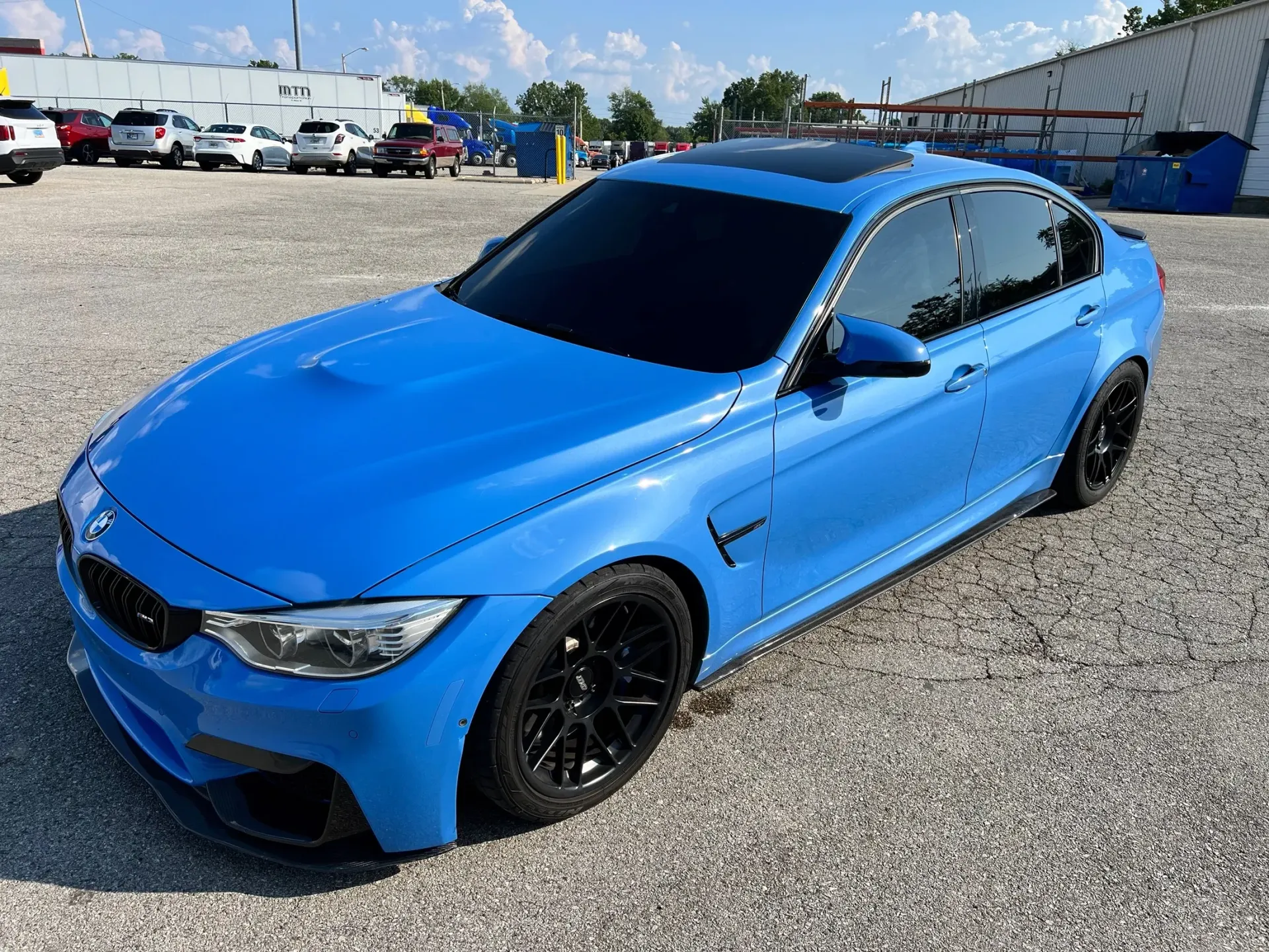 Bright blue sports sedan parked on gravel under a sunny sky
