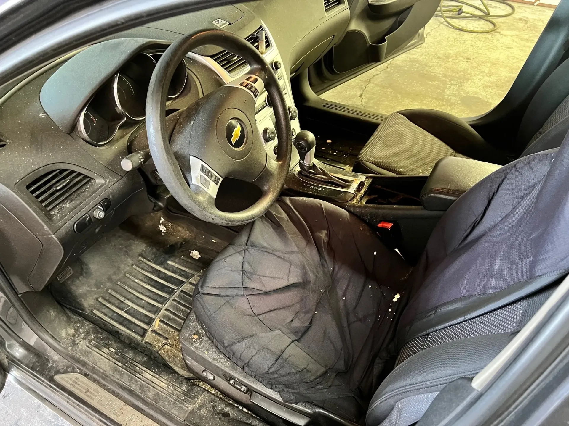 Car interior with steering wheel and seats covered in mud and debris after damage