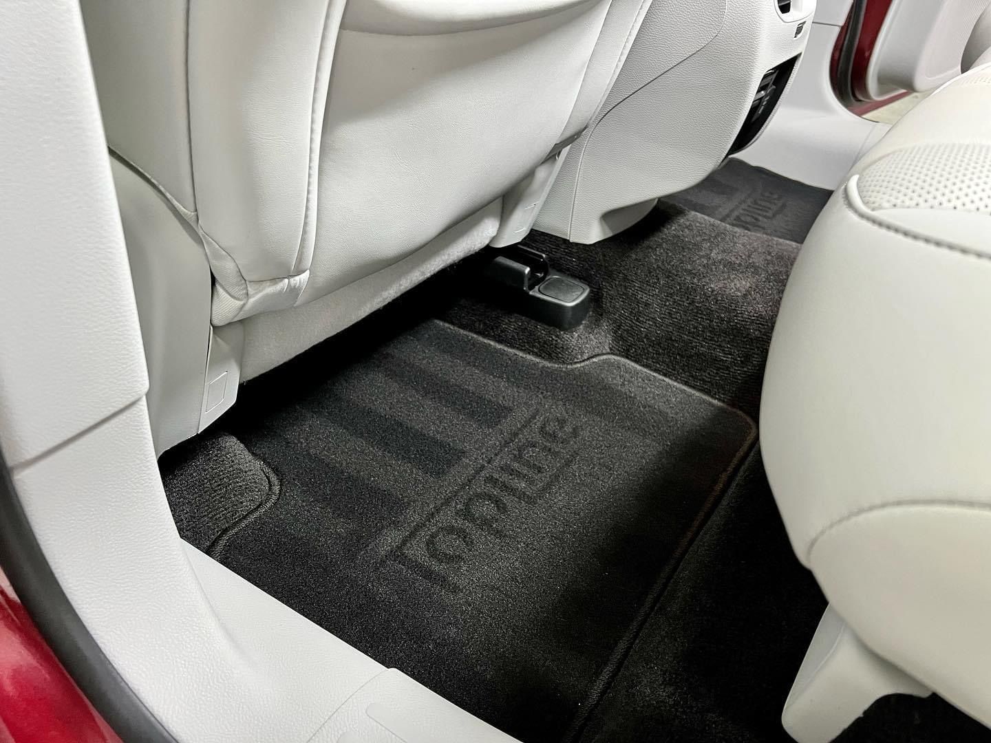 Car floor between two light-colored front seats with black carpeted mats and center console base