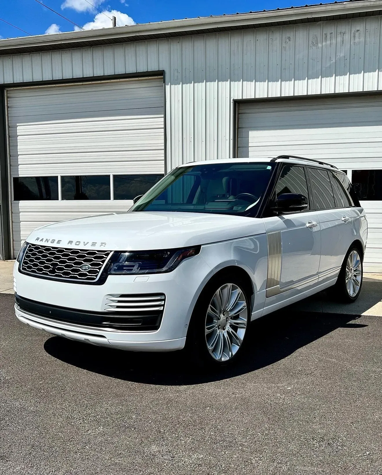 White Range Rover SUV parked outside a garage with white doors on a sunny day