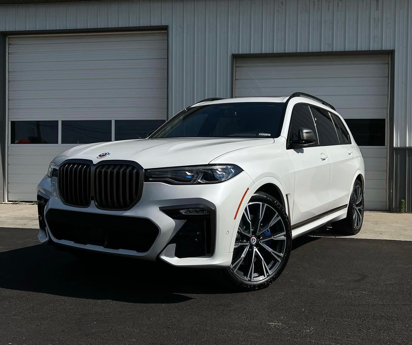 White BMW SUV parked in front of a garage, angled view with black grille and wheels