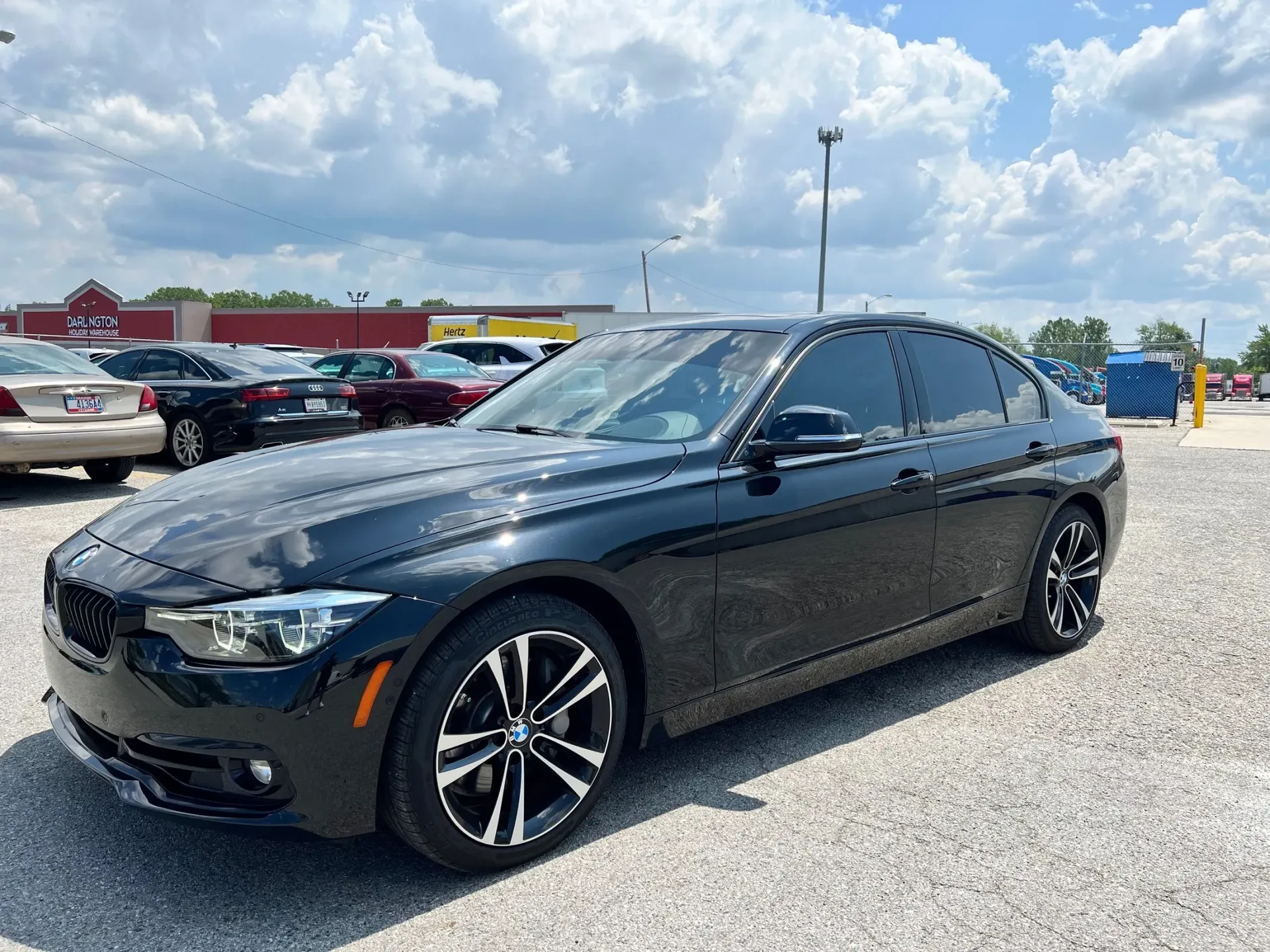 Black sedan parked on gravel lot under a cloudy sky