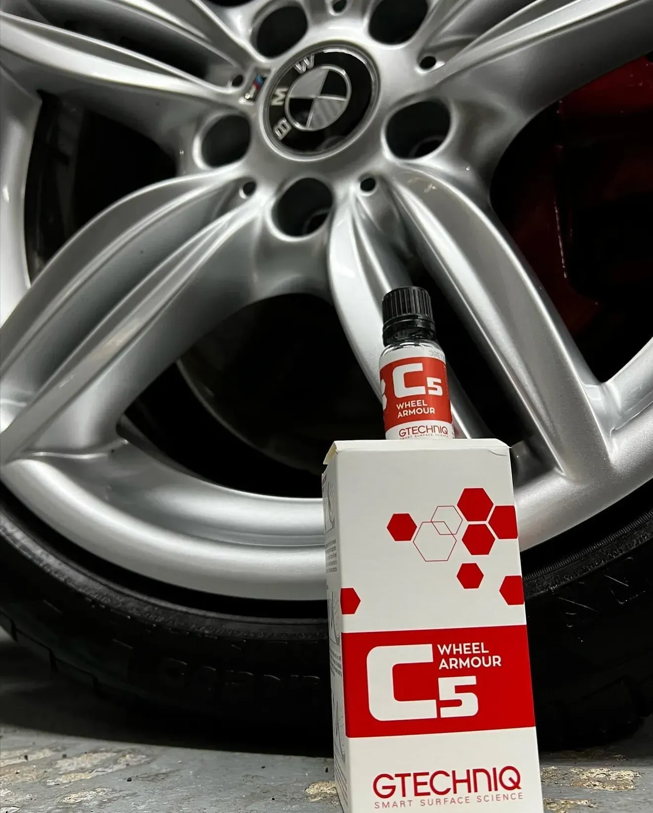 GTX oil bottle in front of a silver car wheel on black tire, red and white packaging.