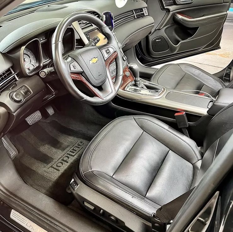 Black leather Chevrolet car interior with steering wheel, center console, and open door view
