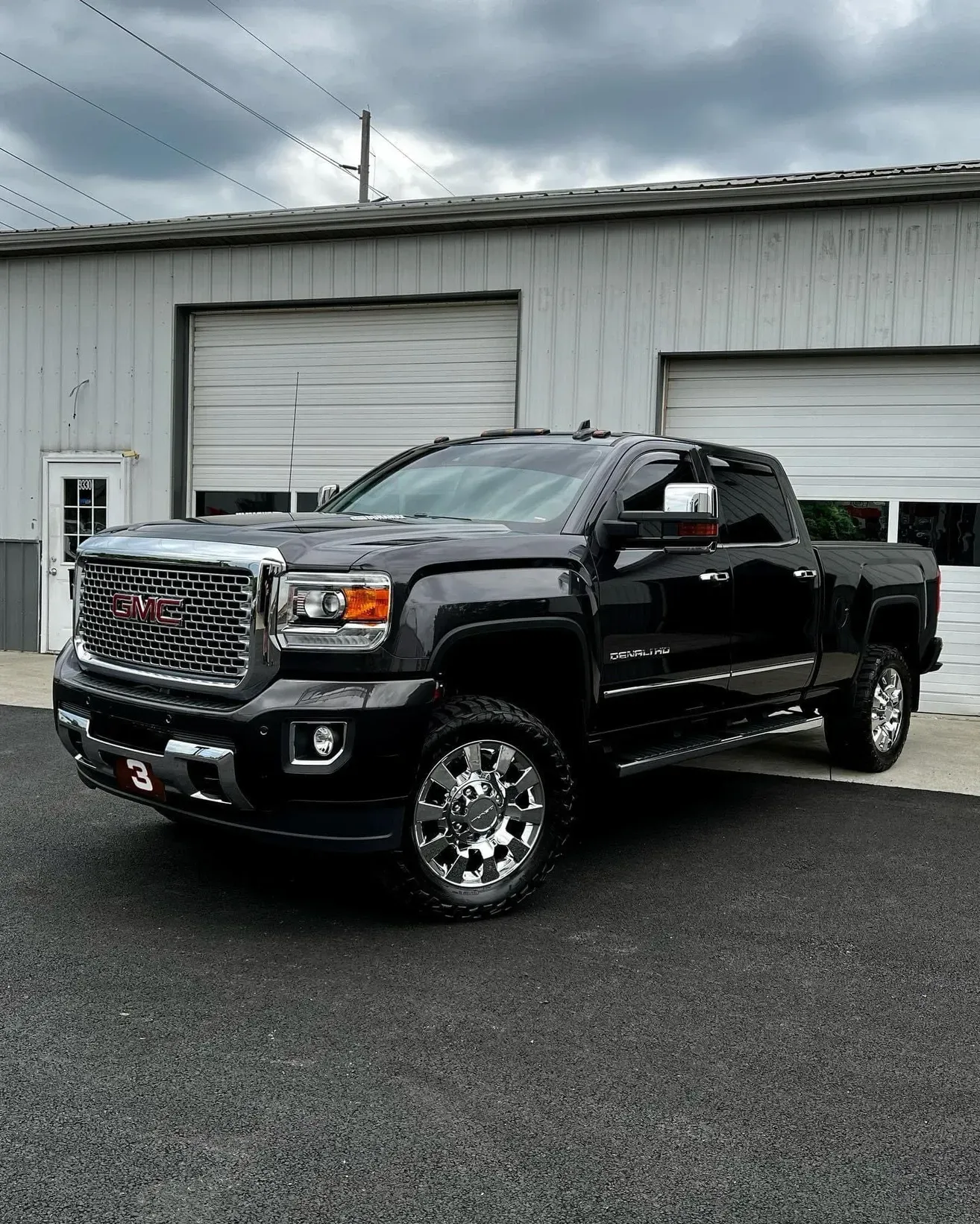 Black GMC pickup truck parked outside a garage on a wet day.