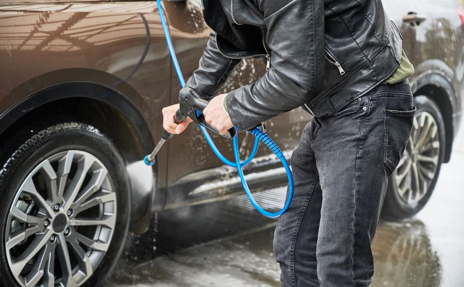 Person pressure-washing a brown SUV with a blue hose outdoors