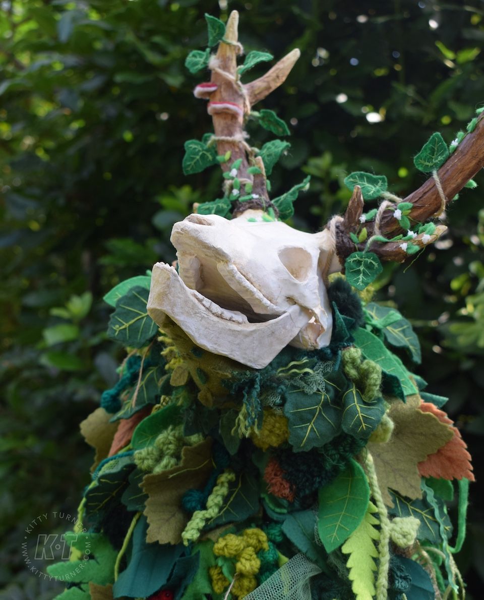 An eco friendly creepy paper mache deer skull puppet covered in green handmade textile leaves.