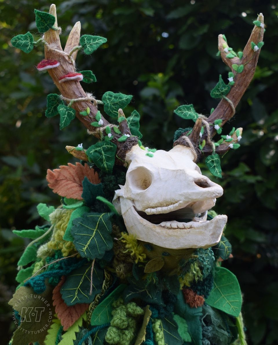An eco friendly creepy paper mache deer skull puppet covered in green handmade textile leaves.
