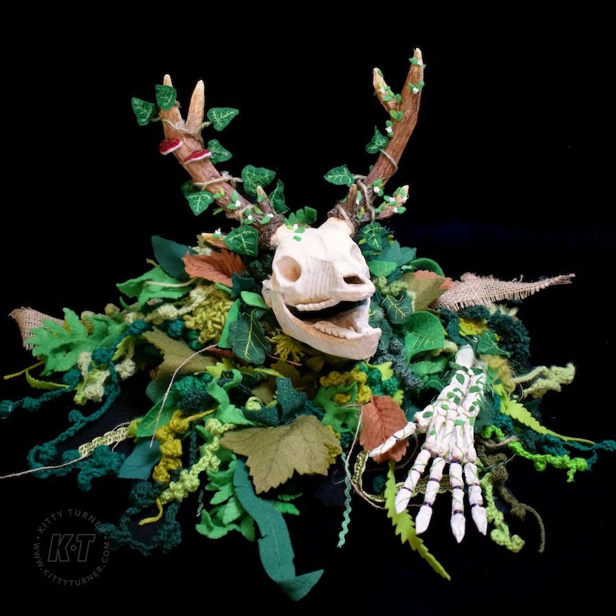 An eco friendly creepy paper mache deer skull puppet covered in green handmade textile leaves.