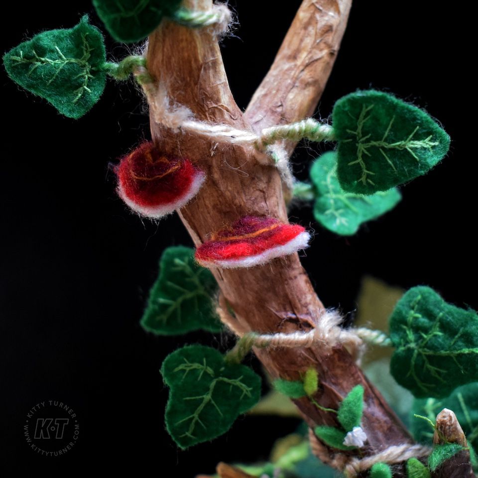 A close up of red needle felted mushrooms on a paper mache antler. With handmade embroidered ivy leaves winding around it. 