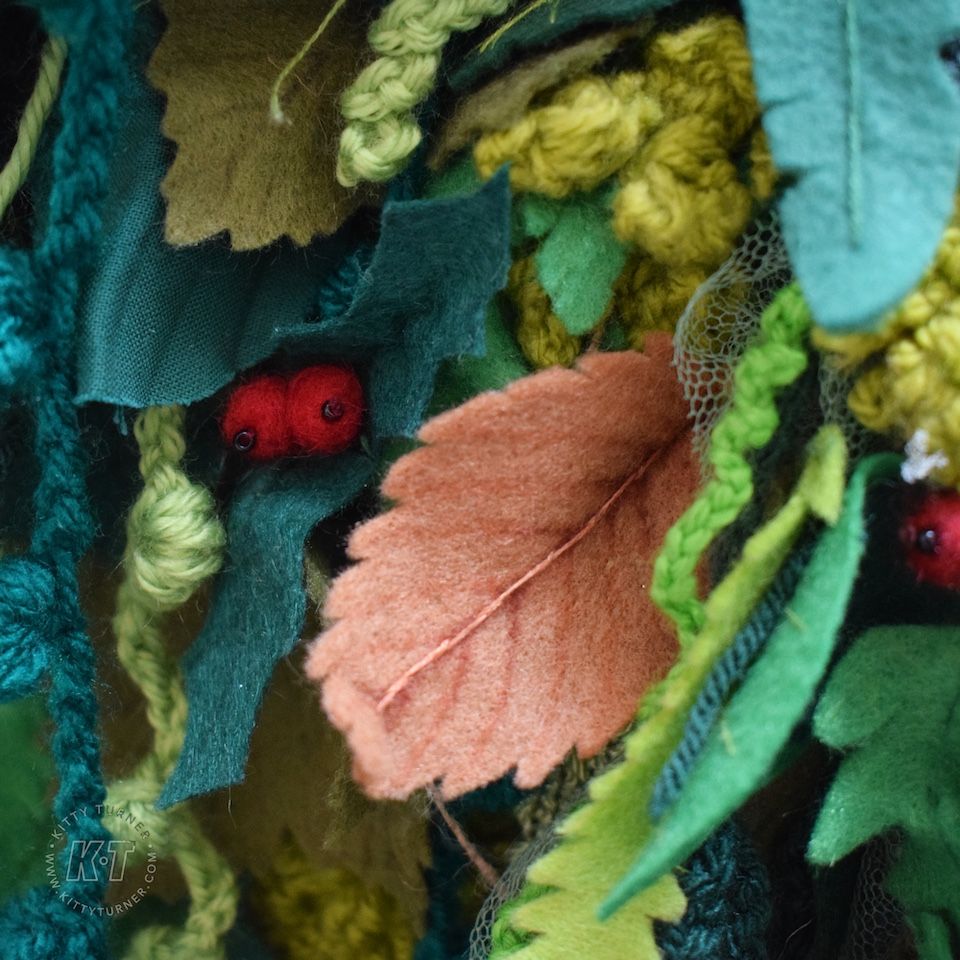 Close up of handmade textile leaves made from felt, net, crochet and wool. Includes greenery, brown leaves and berries.