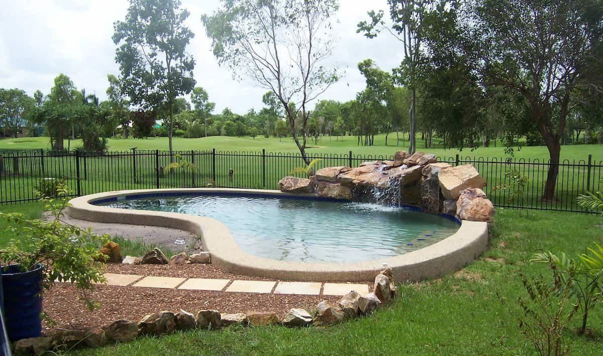 Swimming Pool With Waterfall Feature, Surrounded by Lawn and a Black Fence — Rod Hardy Plunge Pools in Howard Springs, NT
