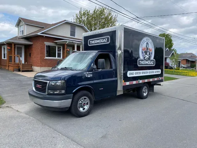 Une camionnette GMC bleue est garée devant une maison en briques.