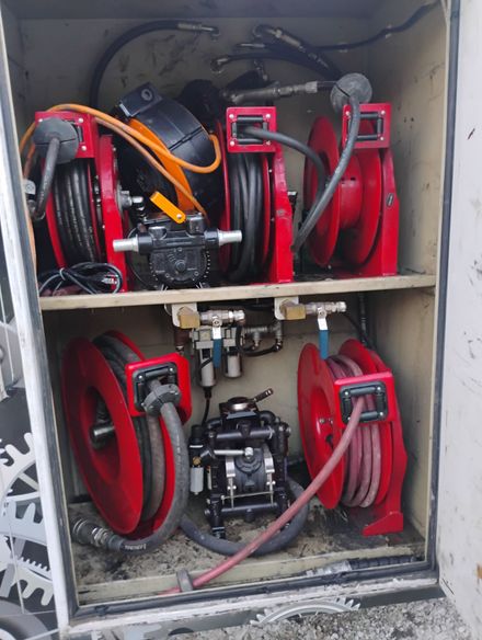 Fire hose cabinet with red hoses and nozzles mounted on shelves inside a metal enclosure