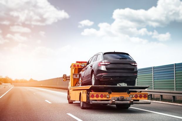 Black car on a tow truck driving on a highway at sunset
