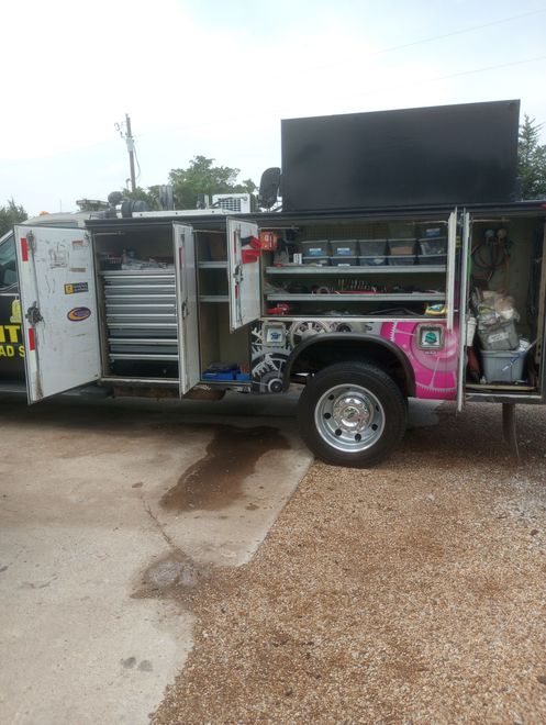 Open utility truck with side compartments and a large black rooftop panel on a gravel lot