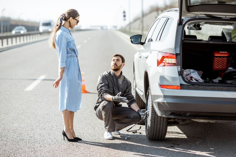 Woman and mechanic beside a white SUV with open trunk on the roadside