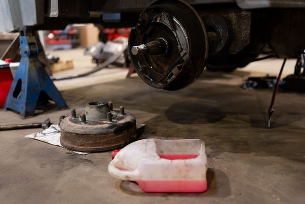 Car wheel hub and brake parts removed on a garage floor with a red drain pan underneath