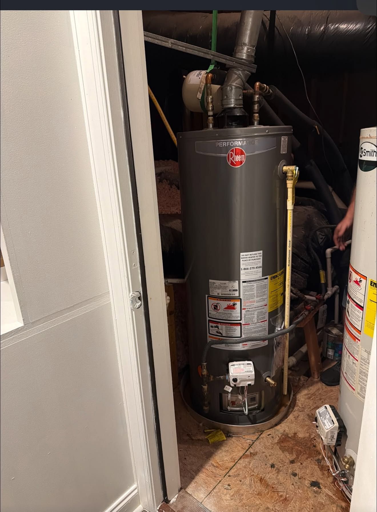 Water heater in a narrow utility closet beside a wall and doorway.