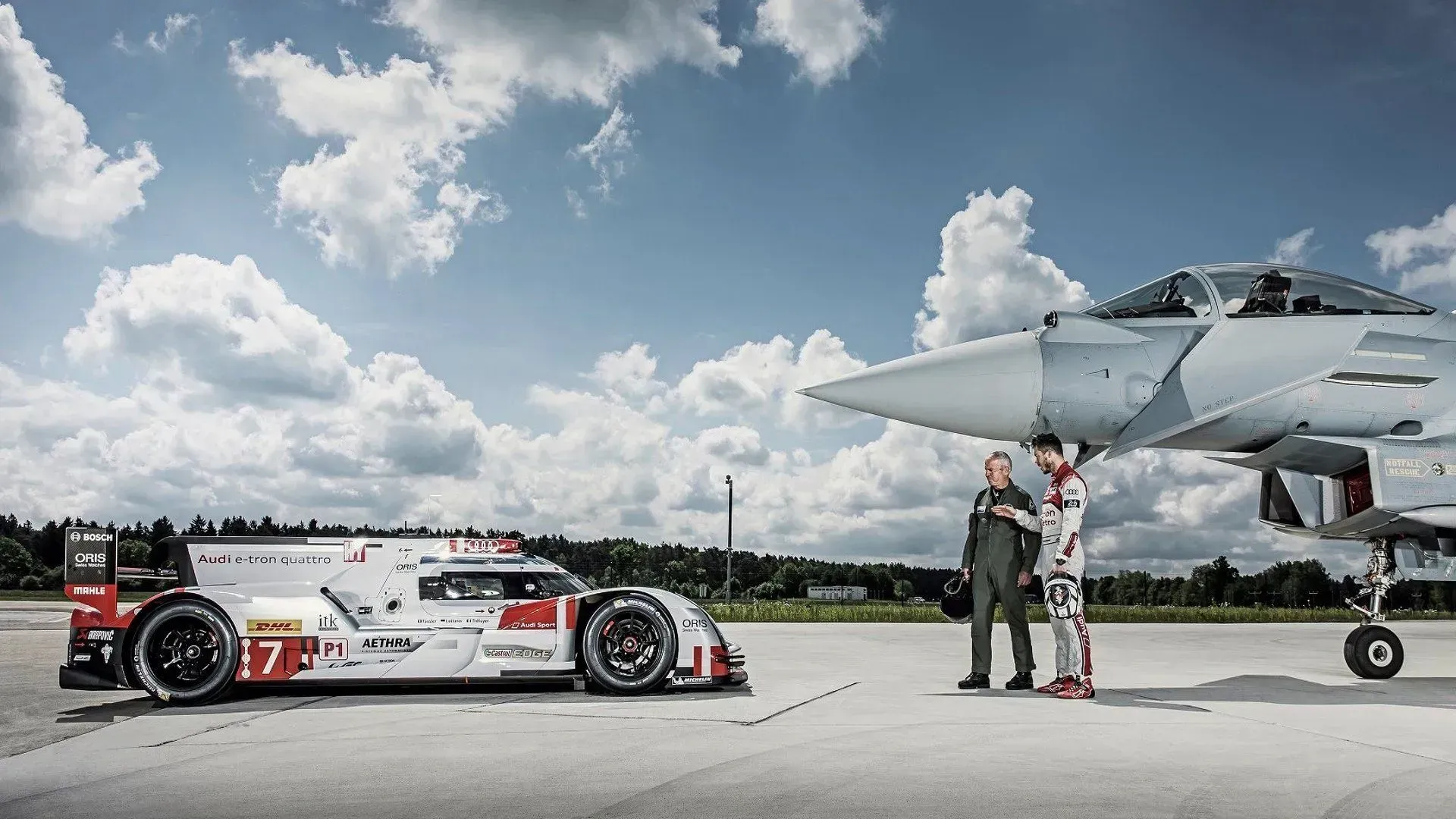 two people standing in between a fighter jet and a race car