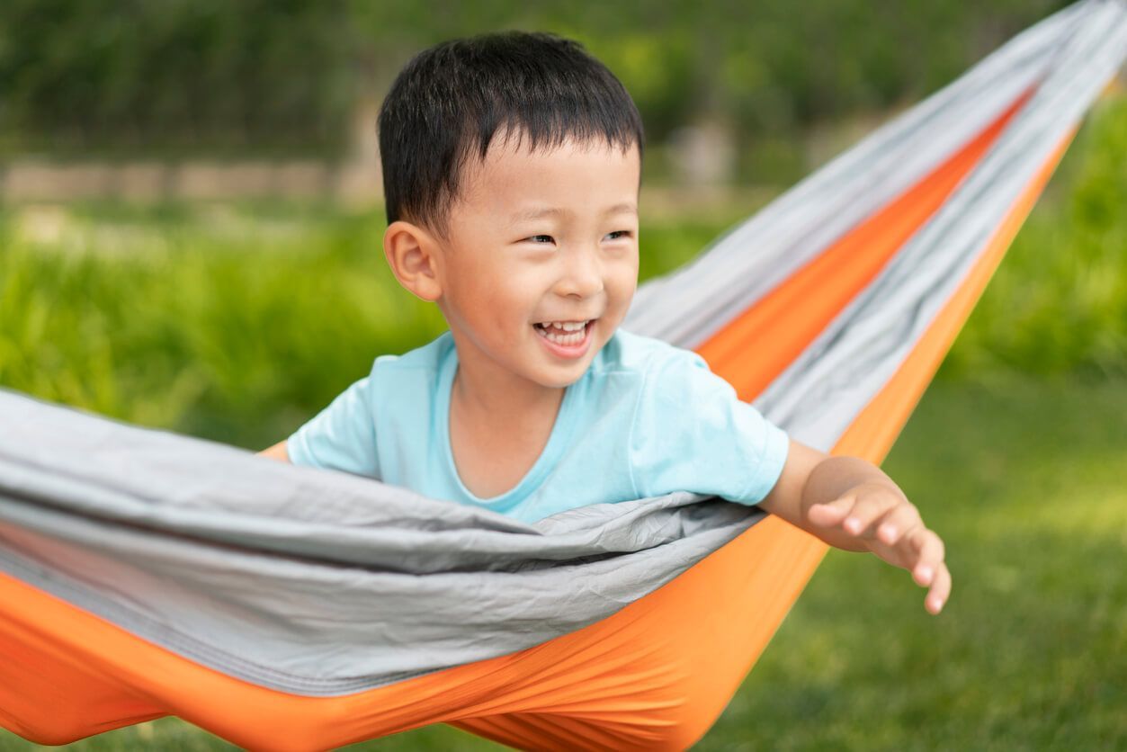 Boy smiling in an orange and gray hammock outdoors.