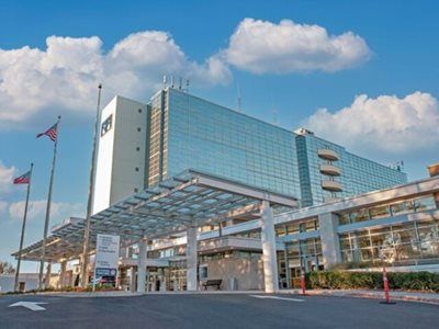 Modern glass and white building, hospital entrance, flags, blue sky.