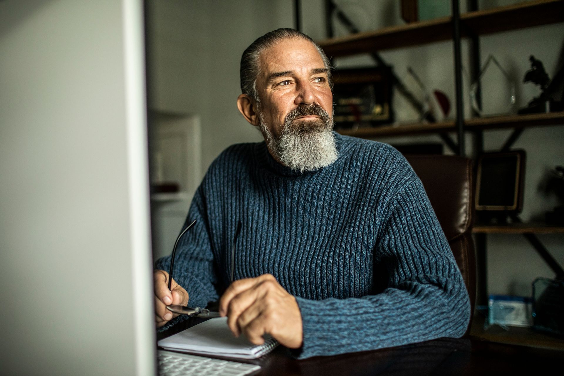 A man with a beard is sitting at a desk in front of a computer.