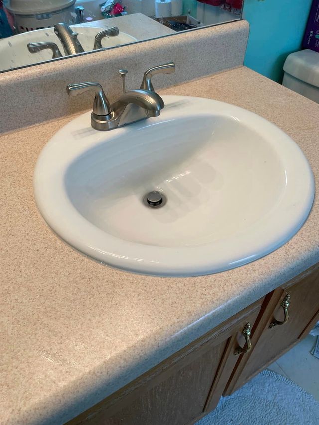 Bathroom sink with chrome faucet and white basin on a speckled countertop, with a mirror above.