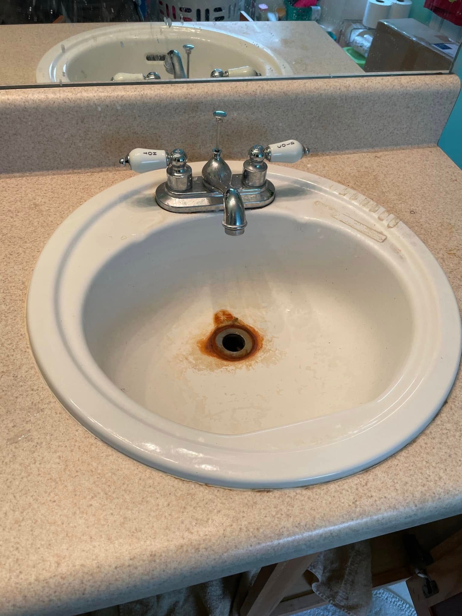 Bathroom sink with rust-stained drain and chrome faucet, seen in a mirror reflection