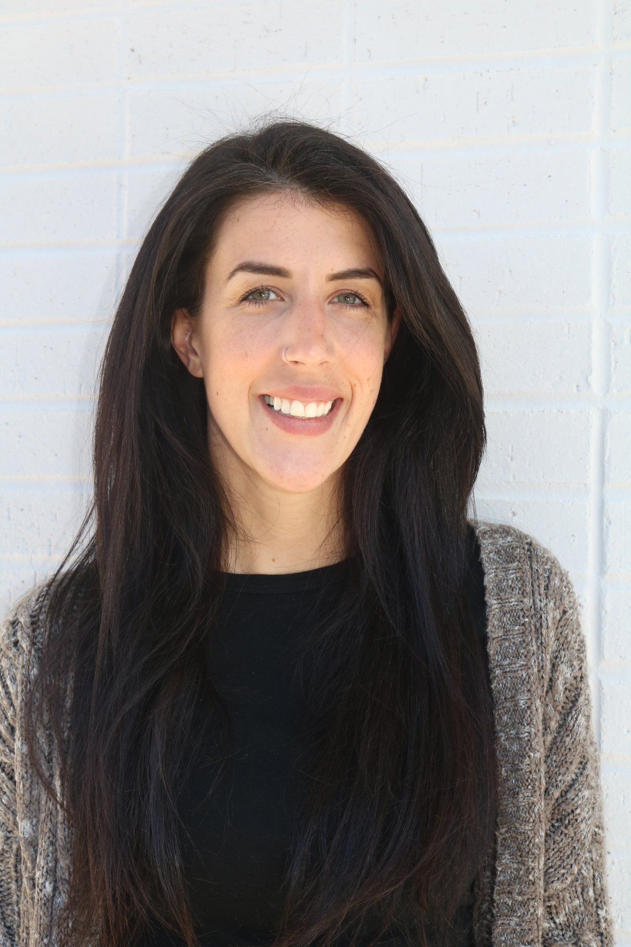A woman with long dark hair is smiling in front of a white wall.