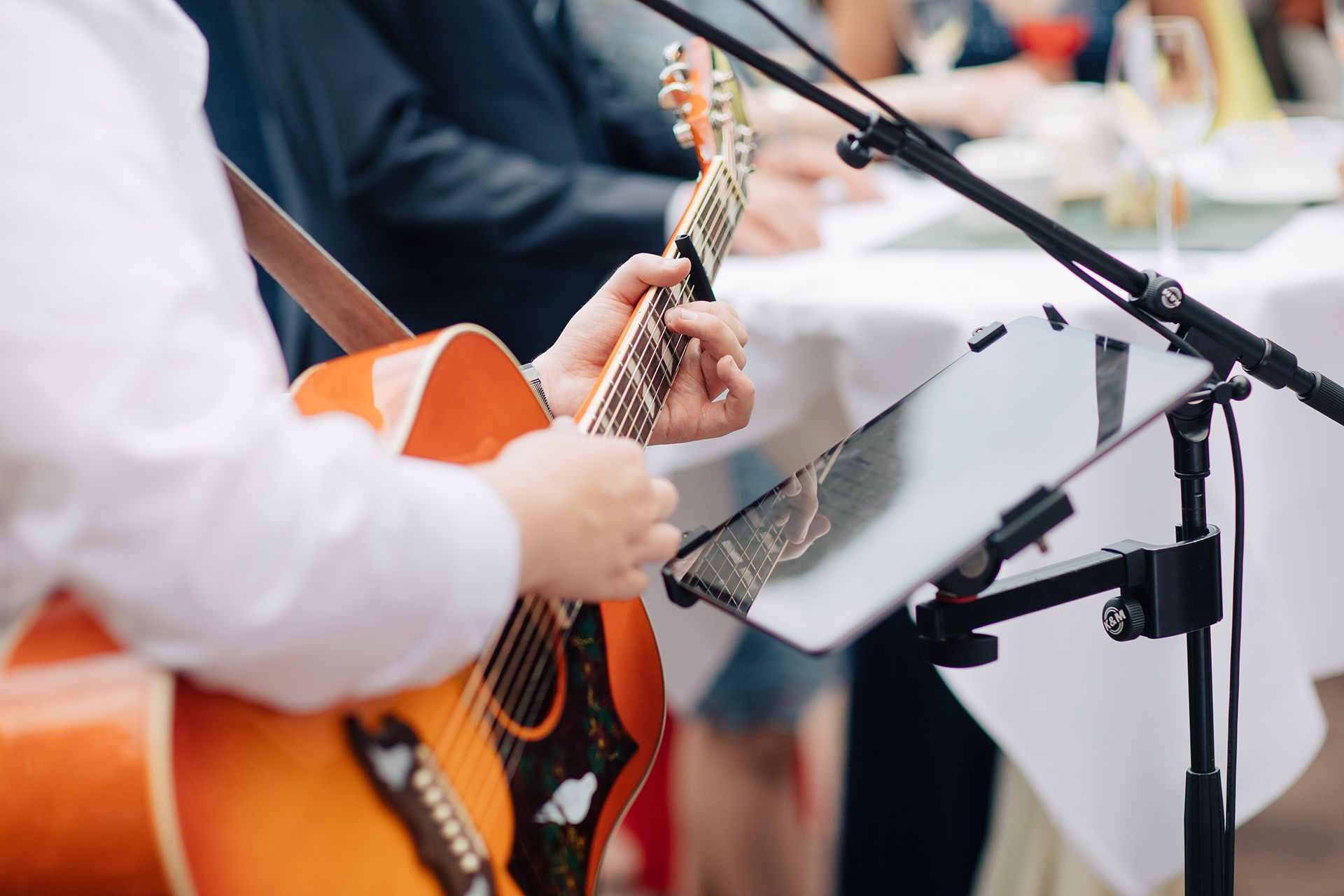 Musician playing orange acoustic guitar beside a microphone and sheet music stand