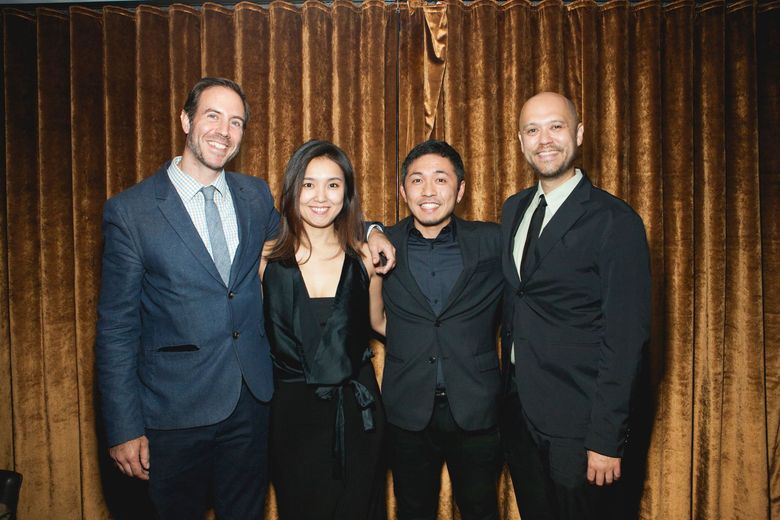 Four people posing in formal attire in front of a gold curtain backdrop.