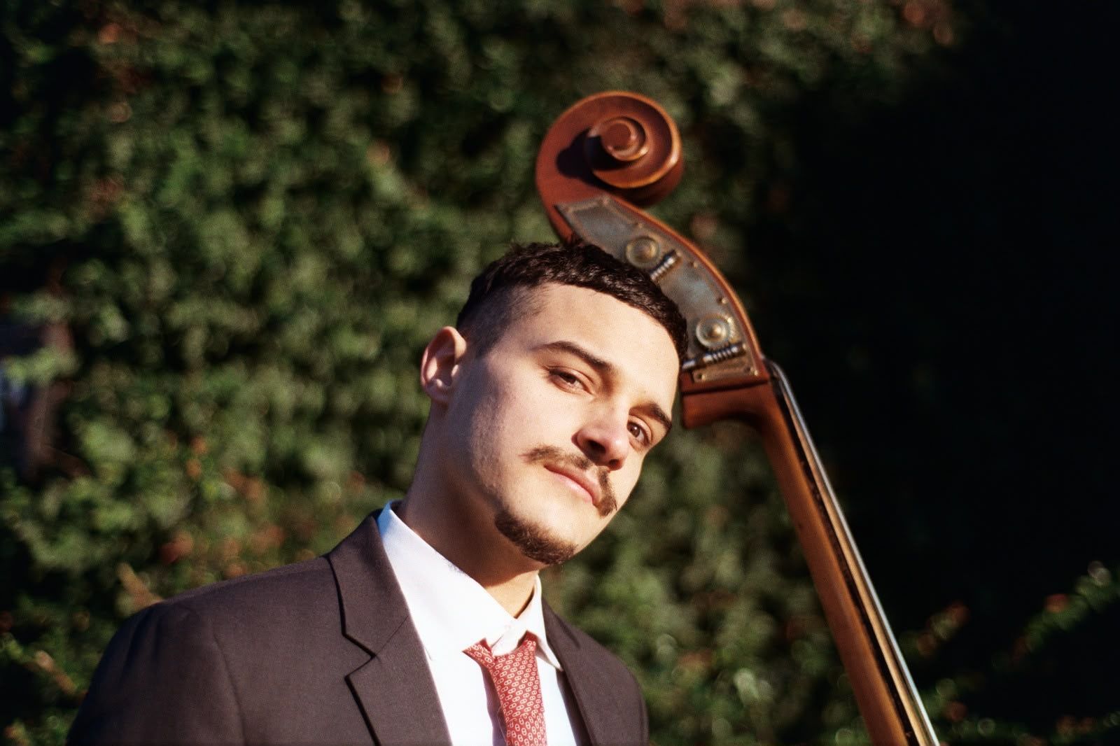 Man in a suit and red tie standing beside an upright bass outdoors