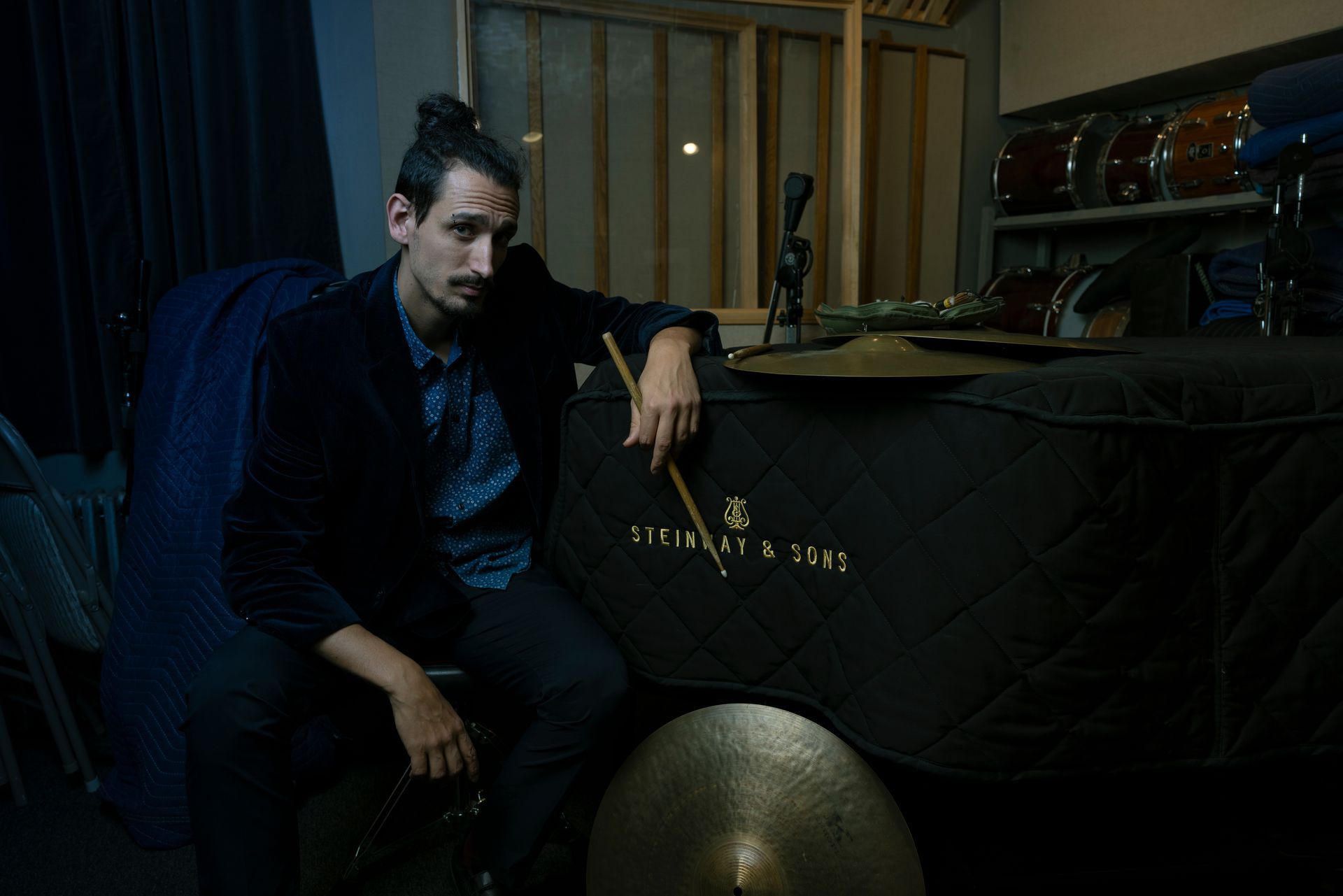 Man sitting on a couch in a dimly lit room beside a keyboard and draped table.